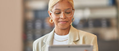 A person with short blond hair and glasses smiles while using a tablet.