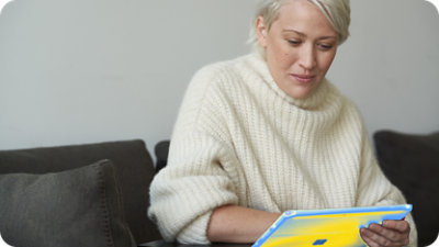 A woman in a white sweater looking at a tablet.