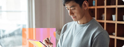 A man wearing a grey shirt looking down while writing in a book.