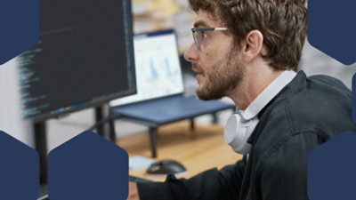 A man wearing headphones on his neck looking at a computer screen.
