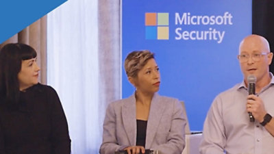 A man and two woman sitting on chairs and addressing media.