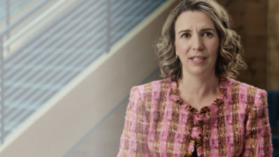 Žena sa kovrdžavom kosom u roze i braon jakni.