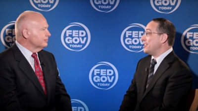 Dva muškarca u odelima razgovaraju, u pozadini se vide natpisi GOV i TODAY.