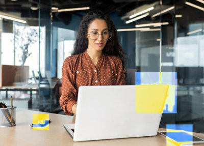 En kvinde iført en orange sweater bruger en bærbar computer, der viser et websted om sikkerhed på skærmen og står på et træbord