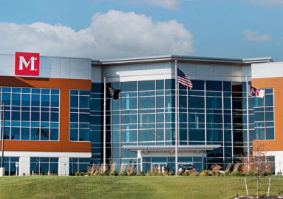 A building with glass windows under a blue sky with clouds, with the letter M visible.