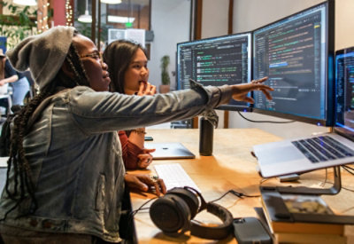 Two women sitting Infront of a computer desk. 