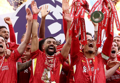 A group of football players celebrating with a man in a red shirt holding up a trophy, and Premier League text visible.