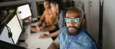 一名戴眼镜的男子坐在桌旁，背景中还有其他人。