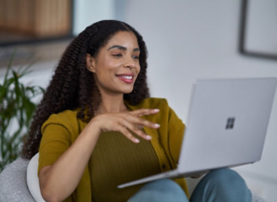 Person seated on a sofa using a laptop, gesturing while working in a modern indoor setting.
