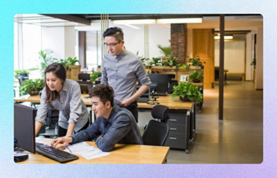 Team reviewing work together at a desk in an open, plant‑filled workspace.