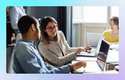Colleagues collaborating at a table using laptops in a bright office.