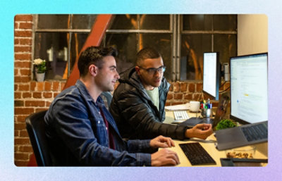 Two coworkers working side by side at dual monitors in an office setting