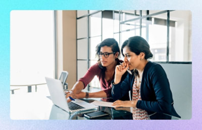 Two colleagues reviewing documents on a laptop at a glass table in a modern office