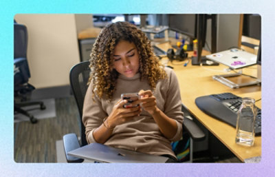 Person seated at desk using smartphone beside computer equipment
