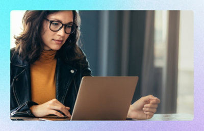 Person using laptop at table in indoor workspace with window light.