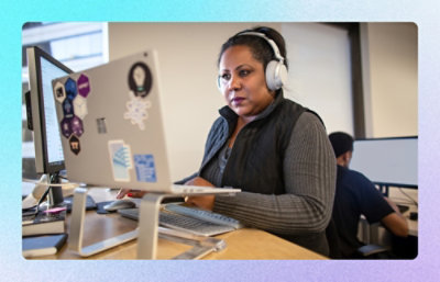Person wearing headphones working at desktop computer in open office workspace.