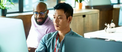 Two persons looking into desktop screen in office.