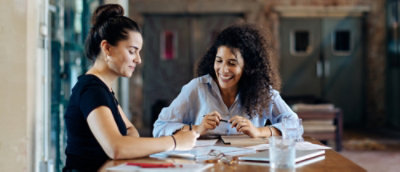 Two women sitting at a table, with one smiling and the other with her hair pulled back.