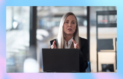Una mujer con el pelo largo y una chaqueta negra hablando con un portátil.