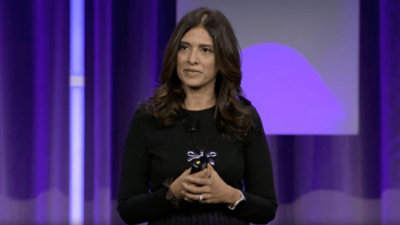 A woman in a black shirt holding a microphone with a purple background.
