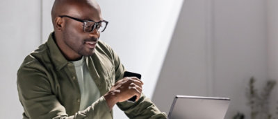 A man holding a mobile and using a laptop.