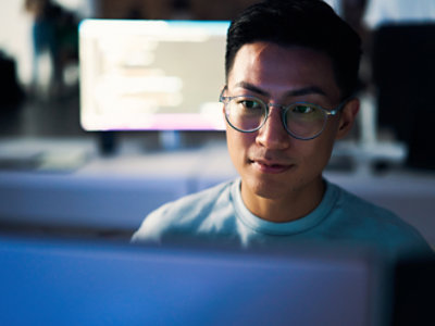 A man wearing glasses looking at a computer screen.