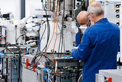 Men in a factory wearing blue overalls and gloves, working on a machine.