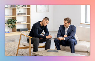 A man in a suit holding a paper while another man sits in a chair.