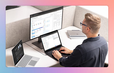 A man sitting at a desk using a laptop with two computers.