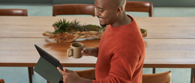 איש מחזיק ספל קפה ומביט בטאבלט.