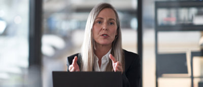 אישה יושבת ליד שולחן ועובדת על מחשב נישא ומסבירה