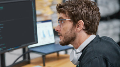 גבר עם משקפיים ואוזניות מביט במסך מחשב.