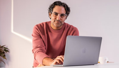 Person in a pink sweater working on a silver laptop at a desk with a coffee cup.