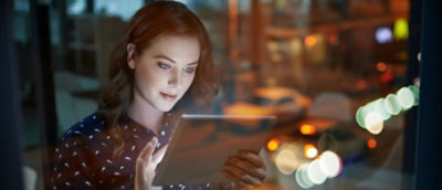 A woman standing in the dark and looking at the tablet.