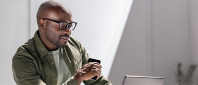 Person holding a smartphone while working on a laptop at a desk.