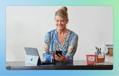 坐在膝上型電腦桌前，看著手機的人。