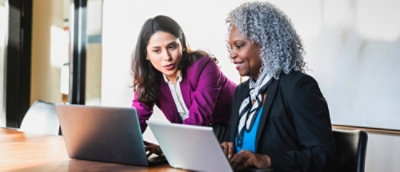Two womens sitting infront of laptop looking side and laughing with one women face blurr