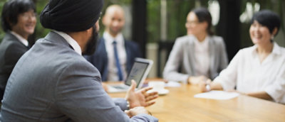 A diverse group of five professionals in business attire are engaged in a meeting around a wooden table.
