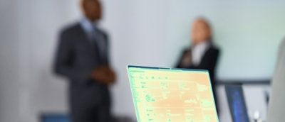 Two people are discussing behined a laptop screen.