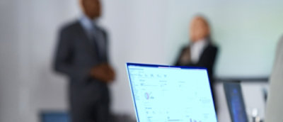Closeup of a laptop screen and two people standing behind it