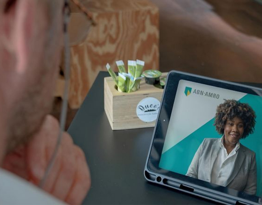 Uma pessoa assistindo a uma apresentação de negócios em um tablet com uma palestrante do ABN-AMRO.