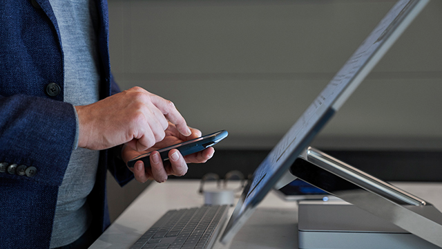 A person in a blue blazer operates a smartphone beside a sleek desktop setup. 