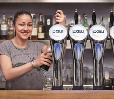 Ein Barkeeper füllt ein Glas aus einem Fassbier-Zapfhahn in einer Bar mit Spirituosenflaschen 