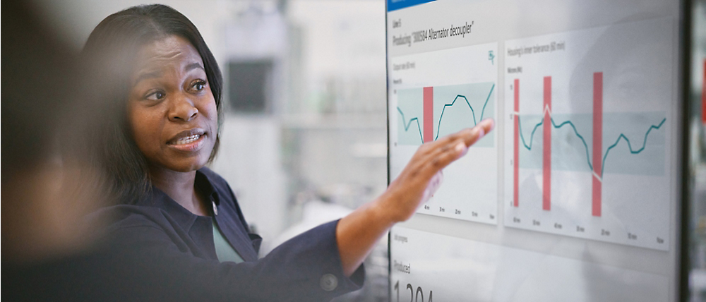 Una mujer profesional presenta datos financieros en una pantalla digital, señalando gráficos y tablas durante una reunión.