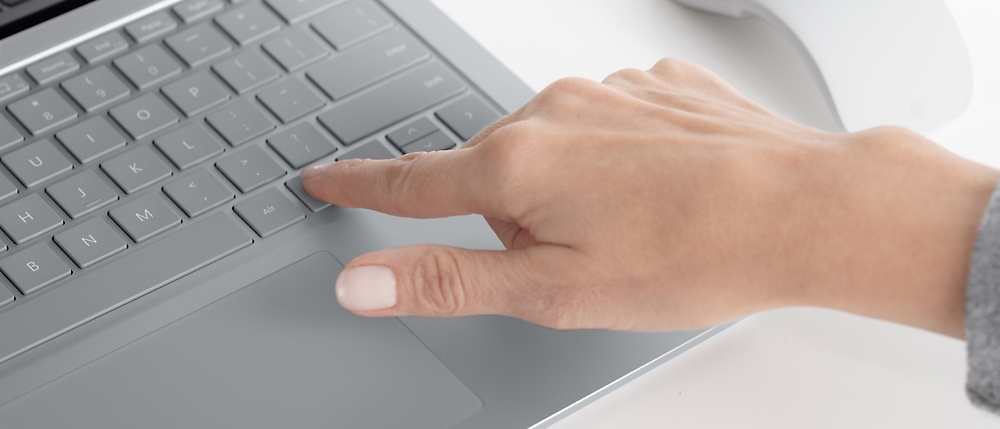 Lähikuva kannettavan tietokoneen kosketusalustaa käyttävän henkilön kädestä.