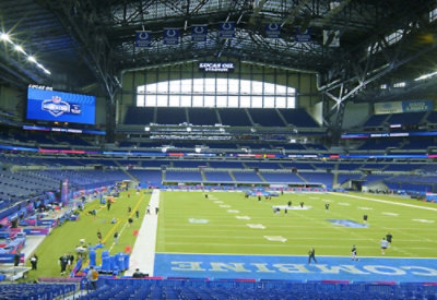 Interior view of Lucas Oil Stadium with a football field prepared for the NFL Combine, large screens, and empty seating areas.