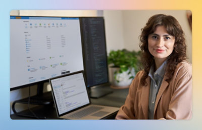 A woman sitting at a desk with two computers.