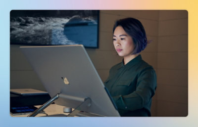 A woman sitting at a computer with a laptop on a stand.