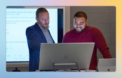 A man standing next to another man looking at a computer.