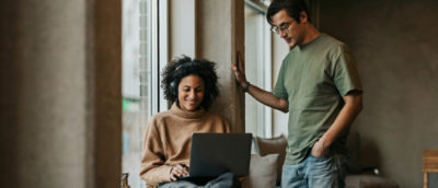 A man standing next to a woman using a laptop.